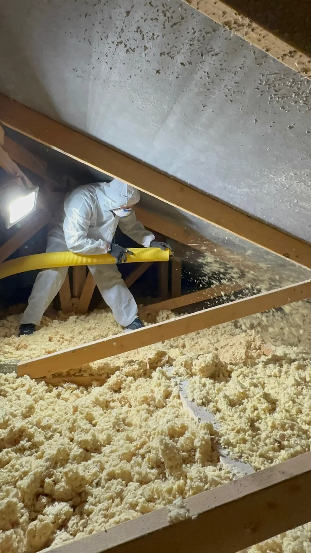 Instalátor v ochranném obleku fukuje izolaci ze skelné vaty na půdě rodinného domu